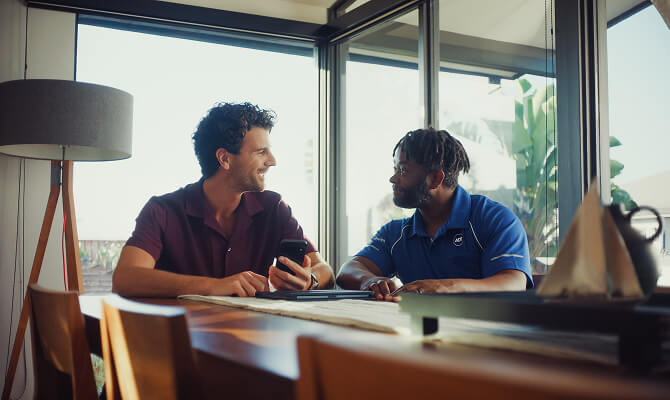 An ADT professional sits at a table with a homeowner, professional installation information together on a mobile device.